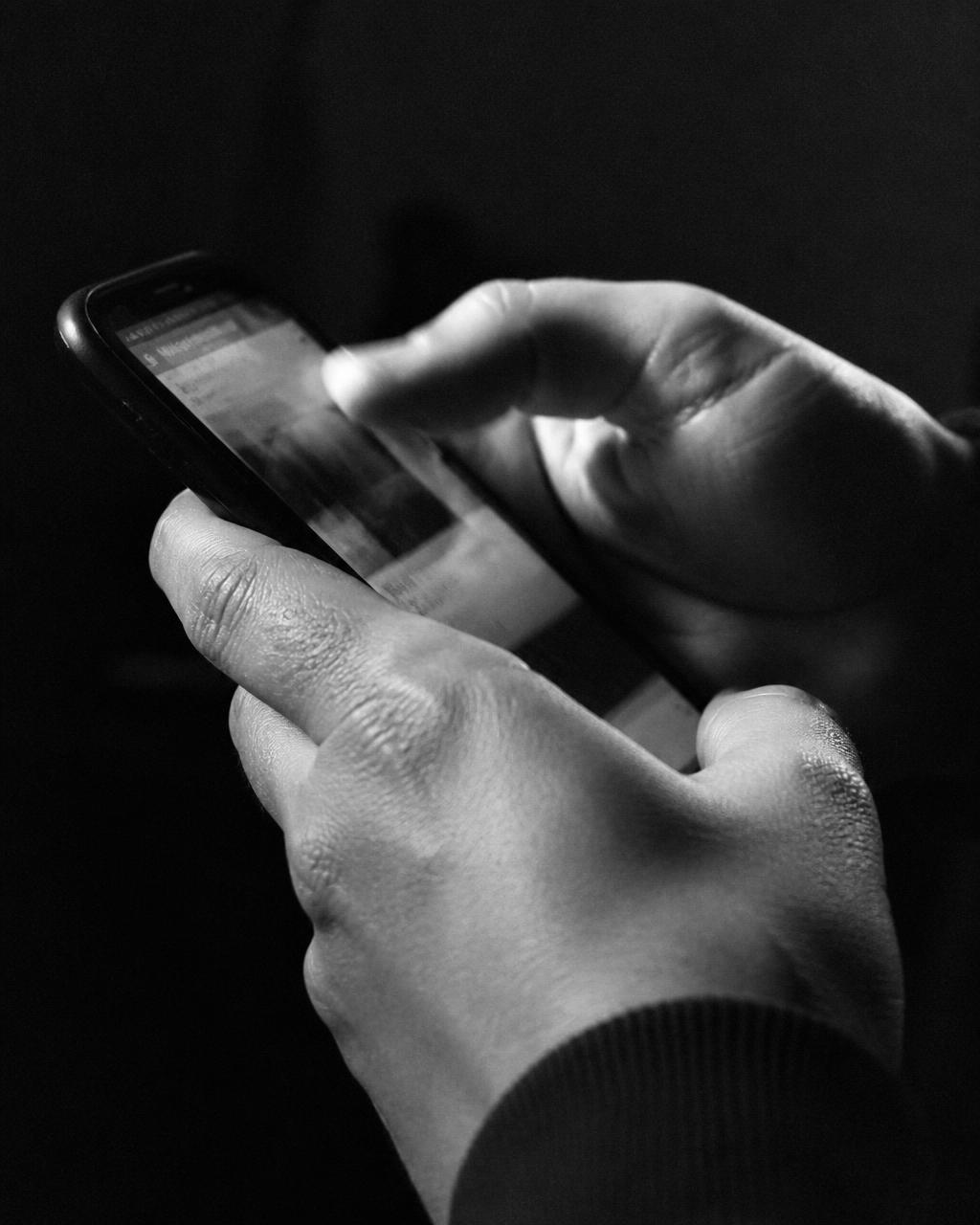 Hands scrolling a phone in dramatic black and white light